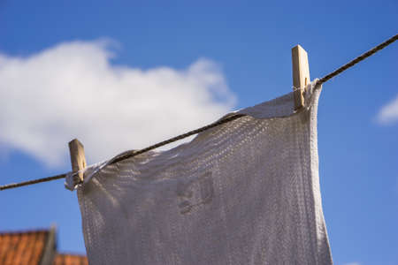 Closeup of white laundry hanging out against the blue sky with old-fashioned wooden clips