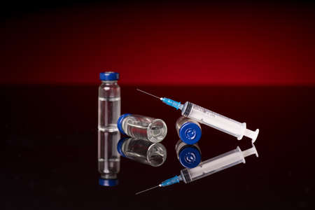 Syringe and medical vials isolated on red dark background with glossy reflectionの写真素材