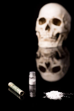 cocaine or other illegal drugs that are sniffed by means of a tube and Skull, isolated on black glossy backgroundの写真素材