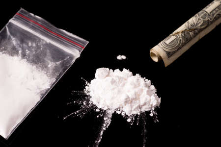 cocaine, Herion or other illegal drugs that are sniffed by means of a tube or injected with a syringe and money, isolated on black glossy backgroundの写真素材