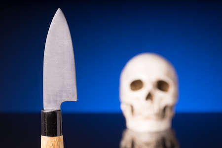 knife and blurry skull isolated on black blue background med reflectionの写真素材