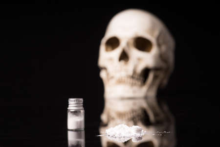 cocaine or other illegal drugs that are sniffed by means of a tube and Skull, isolated on black glossy backgroundの写真素材