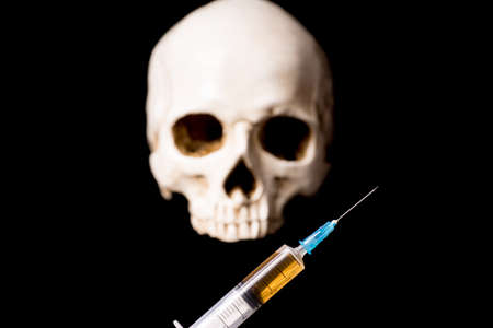 Syringe with brown liquid and blurry skull isolated on black backgroundの写真素材