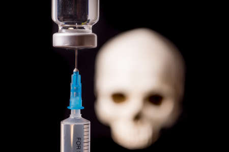 medical vials and syringe with blurry skull isolated on black backgroundの写真素材