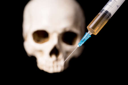 Syringe with brown liquid and blurry skull isolated on black backgroundの写真素材