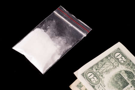 cocaine, Herion or other illegal drugs that are sniffed by means of a tube or injected with a syringe and money, isolated on black glossy backgroundの写真素材