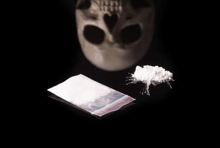 cocaine, Herion or other illegal drugs that are sniffed by means of a tube or injected with a syringe and Skull, isolated on black glossy backgroundの写真素材