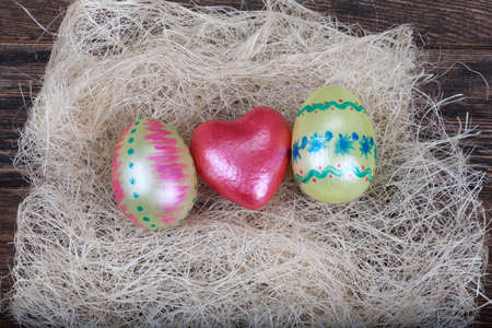 Easter eggs with  red heart symbol in natural nest on wooden background