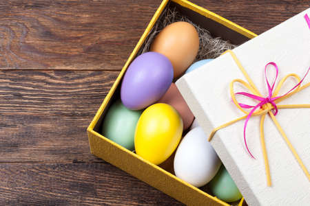 Colorful Easter Eggs decorated in beautiful giftbox with ribbons on wooden background