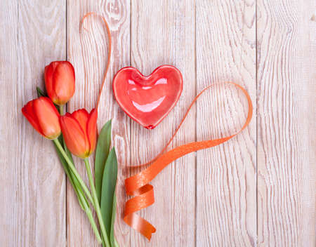 Red heart shaped valentine with tulips and ribbon on wooden backgroundの写真素材