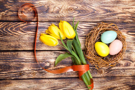 Easter Eggs in a birds nest with colorful tulips on wooden background