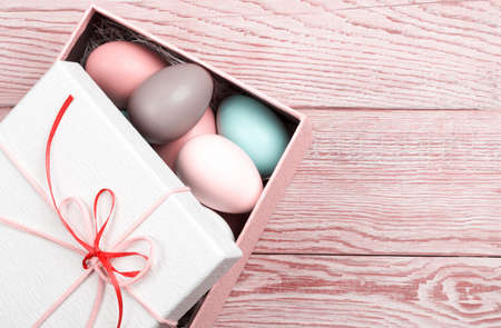 Colorful Easter Eggs decorated in beautiful giftbox with ribbons on wooden background