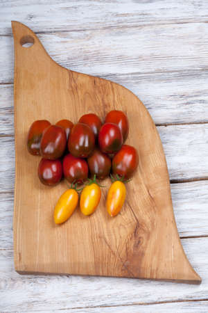 Ripe yellow and chocolate cherry tomatoes on a wooden chopping boardの写真素材