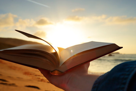 Open book with the pages moved by the air, held by the hand of an unrecognizable person and illuminated by the light of a low sun. Concept of culture and lifestyle. horizontal.の写真素材