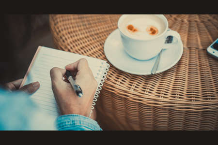 Closeup of a young business woman write a book for work and drinking some coffeeの写真素材