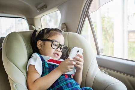 Cute little girl playing smartphone lying on child car seatの写真素材
