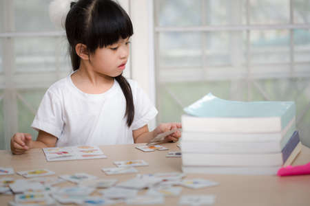 Cute little girl is playing with educational cards while sitting at tableの写真素材