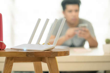 closeup of a wireless router and a man using smartphone on living room at homeの写真素材
