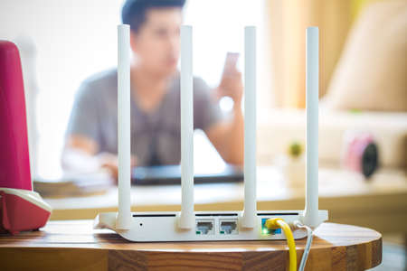 closeup of a wireless router and a man using smartphone on living room at home ofiice