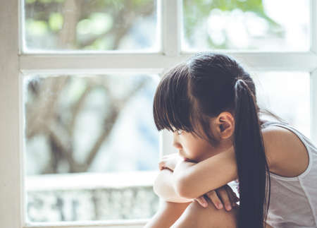 Depressed Little girl  near window at home, closeupの写真素材