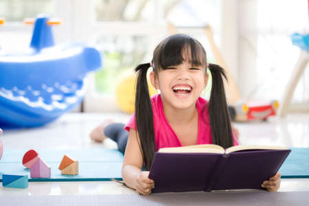 Cute little girl is reading a book . Funny kid having fun in kids roomの写真素材