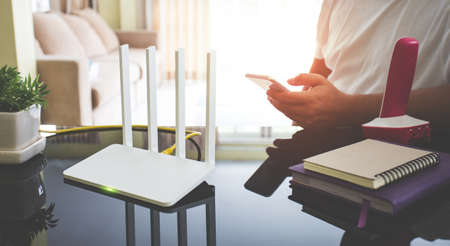 closeup of a wireless router and a young man using smart phone on living room at home