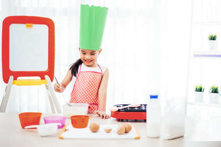 Asian kid having fun with cooking and preparing the dough, bake cookies in the kitchenの写真素材
