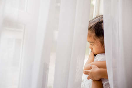 Pretty little girl looking through the windowの写真素材