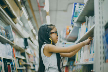 Little Asian child  picking books from the bookshelf の写真素材