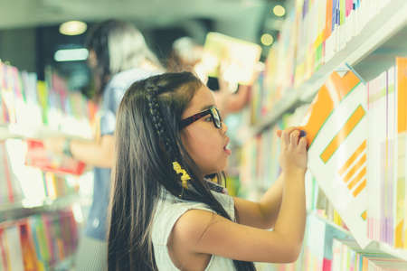 Little Asian child  picking books from the bookshelf の写真素材