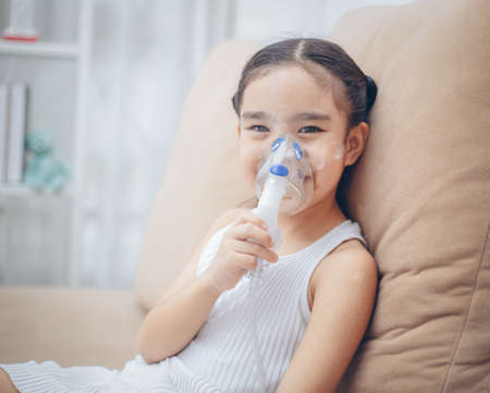 Cute Asian child  patient inhalation therapy by the mask of inhaler with soft stream smoke from bronchodilator.の写真素材