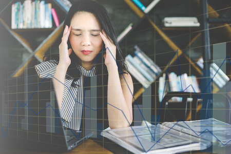 Asian young business girl working Overworked suffering from headache with financial graph report backgroundの写真素材