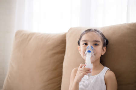 Cute Asian child patient inhalation therapy by the mask of inhaler with soft stream smoke from bronchodilator.の写真素材