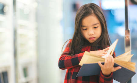 Portrait Asian child holding open textbook in hands in book storeの写真素材