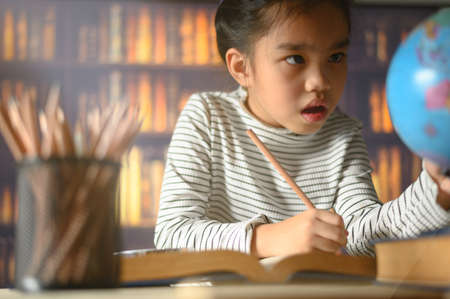 asian child  girl  industrious  is sitting at a desk  indoors. Kid is learning in home