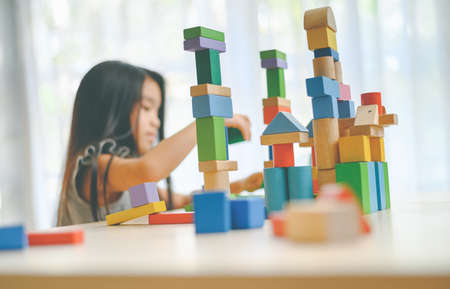 little girl in a colorful shirt playing with construction toy blocks building a tower . Kids playing. Children at day care. Child and toys.の写真素材