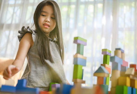 little girl in a colorful shirt playing with construction toy blocks building a tower . Kids playing. Children at day care. Child and toys.の写真素材