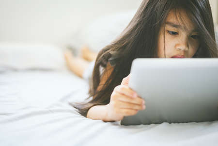Cute child using a tablet and smiling while sitting on sofa at homeの写真素材