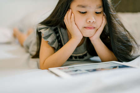 Cute child using a tablet and smiling while sitting on sofa at homeの写真素材