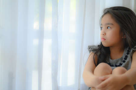 Depressed Little girl near window at home, closeupの写真素材