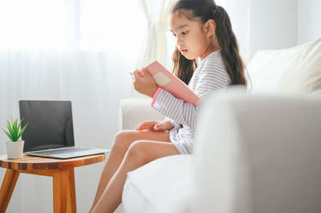 happy child little asian girl  reading a books on the table in the living room at home. family activity conceptの写真素材