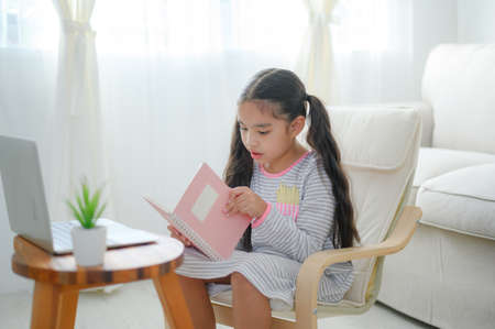 happy child little asian girl  reading a books on the table in the living room at home. family activity conceptの写真素材