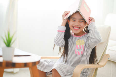 Happy little schoolgirl with book on her head. Back to school concept.の写真素材