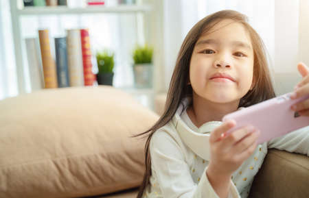Cute little girl using smart phone at homeの写真素材