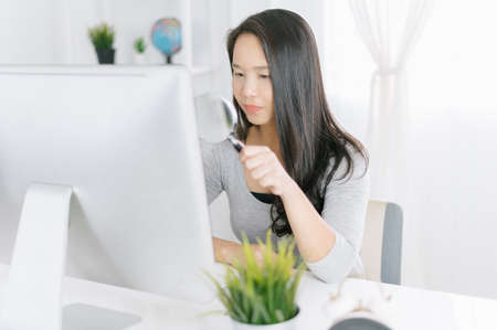 woman with magnifier glass examining a desktop computer. Scanning Files Searching Processing Anti-virus Conceptの写真素材