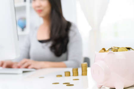 Cute piggy bank with gold coin and blur  Woman working on computer  at  home office background. concept saving money for finance accountingの写真素材