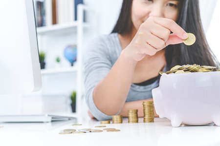 Woman putting golden coin in pink piggy bank. saving money, budget, investment, finance conceptの写真素材
