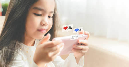 asian child using a smartphone and smiling while sitting on sofa at home, Hand using smartphone with Social media conceptの写真素材