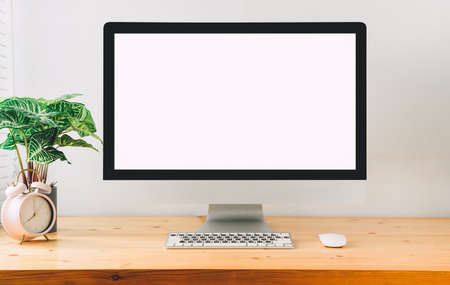workspace with computer with blank white screen, and office supplies on a wooden desk