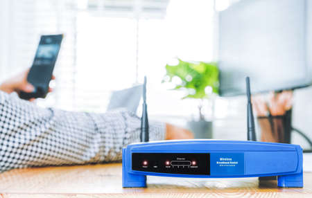 closeup of a wireless router and a man using smartphone on living room at home officeの写真素材